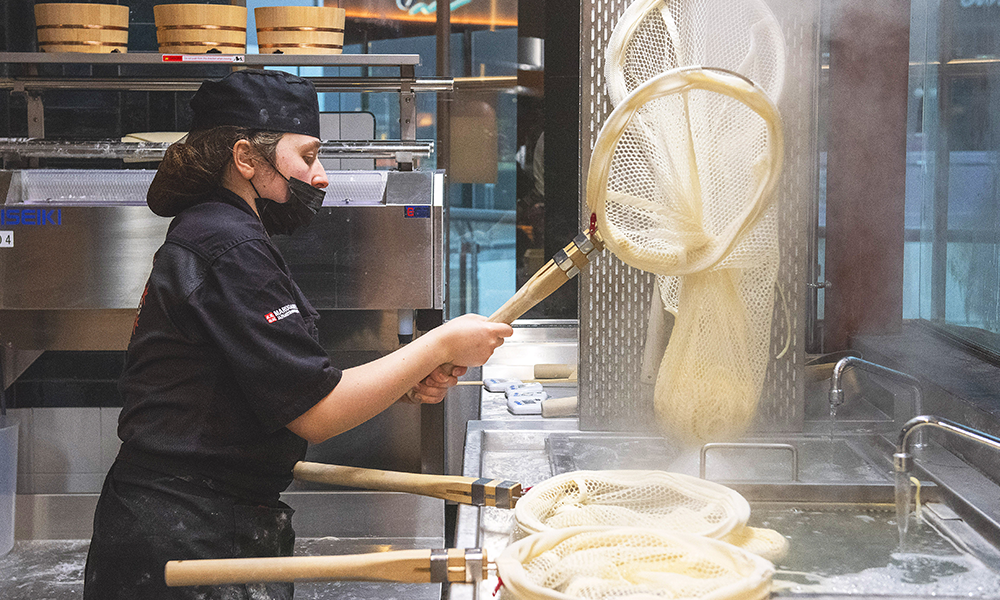 A chef nets freshly cooked udon noodles in the open kitchen