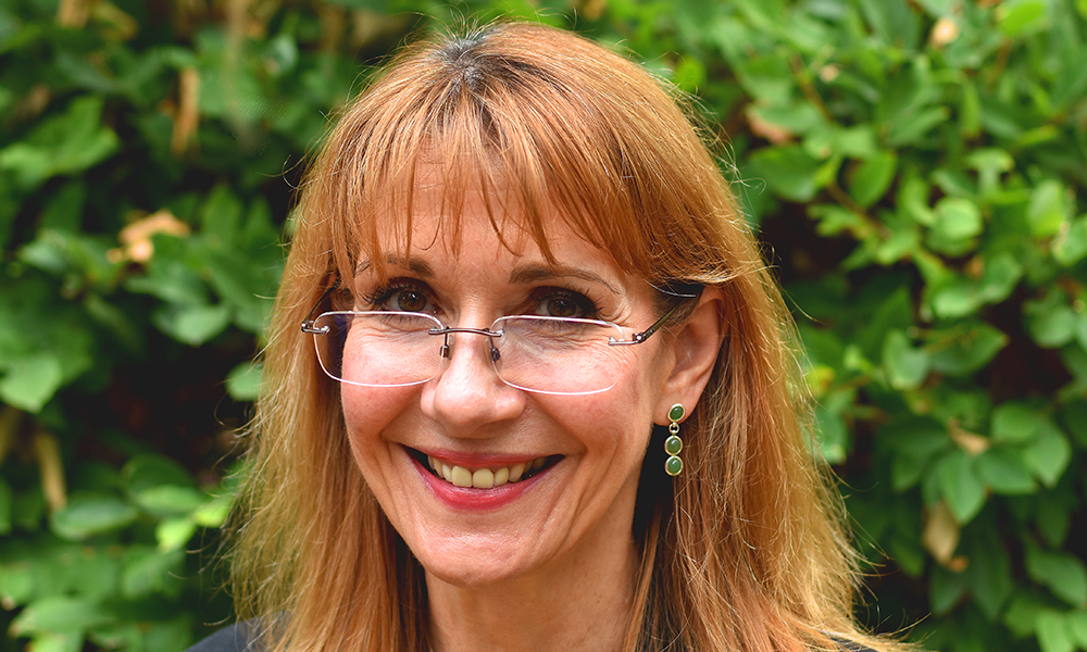 Image shows Janet Smith, a woman with dyed red hair, wearing rimless glasses and gold earrings set with green stones
New City College principal Janet Smith