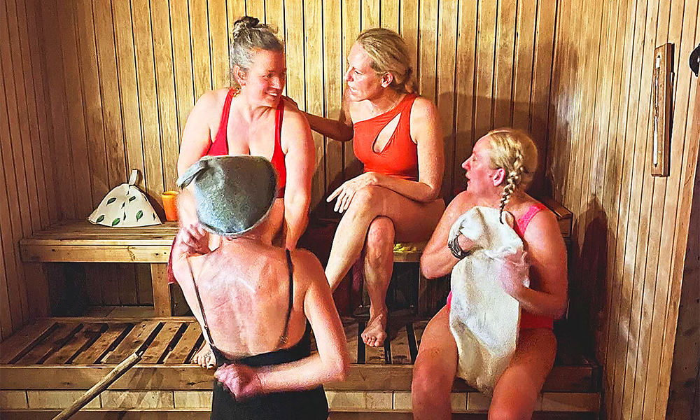 Four women in bathing costumes chat on wooden benches in a sauna 
