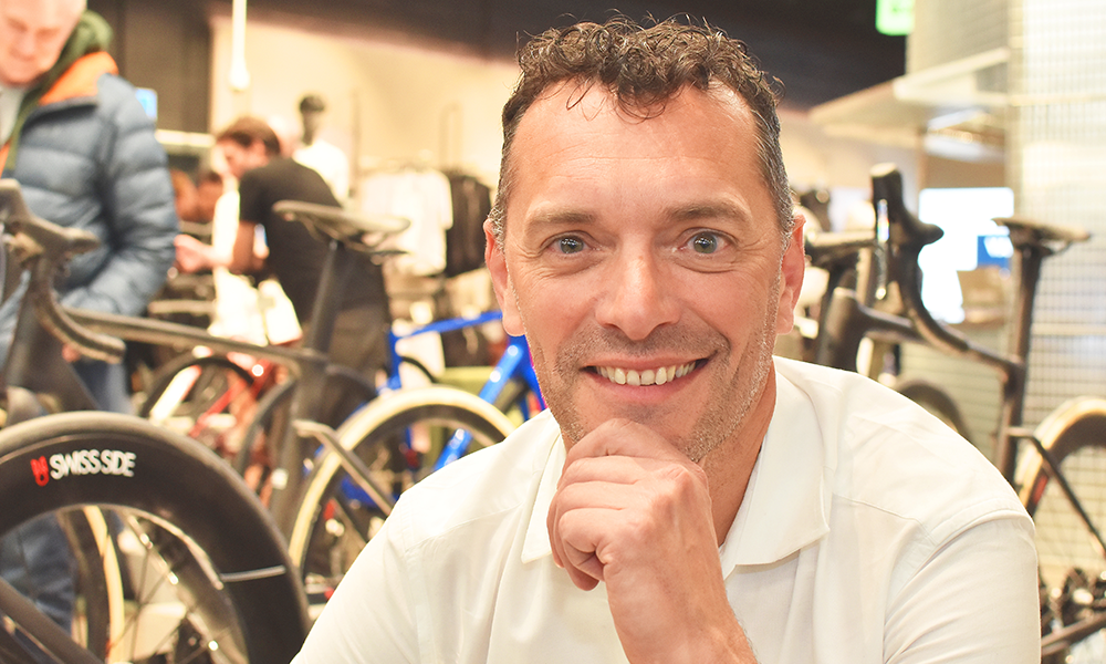 This images is a portrait of Van Rysel founder Nicolas Pierron wearing a white shirt and posing in front of bikes in the store
