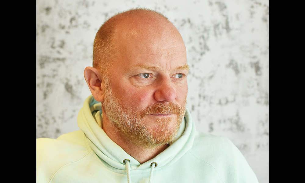 Image shows James Robson of Roe restaurant, a bearded man with blue eyes wearing a light green hoodie in front of a black and white marble background