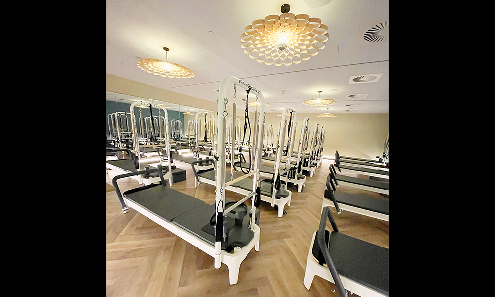 Image shows Reformer Pilates machines in a room with a wooden floor. The machines are cream with black plastic details