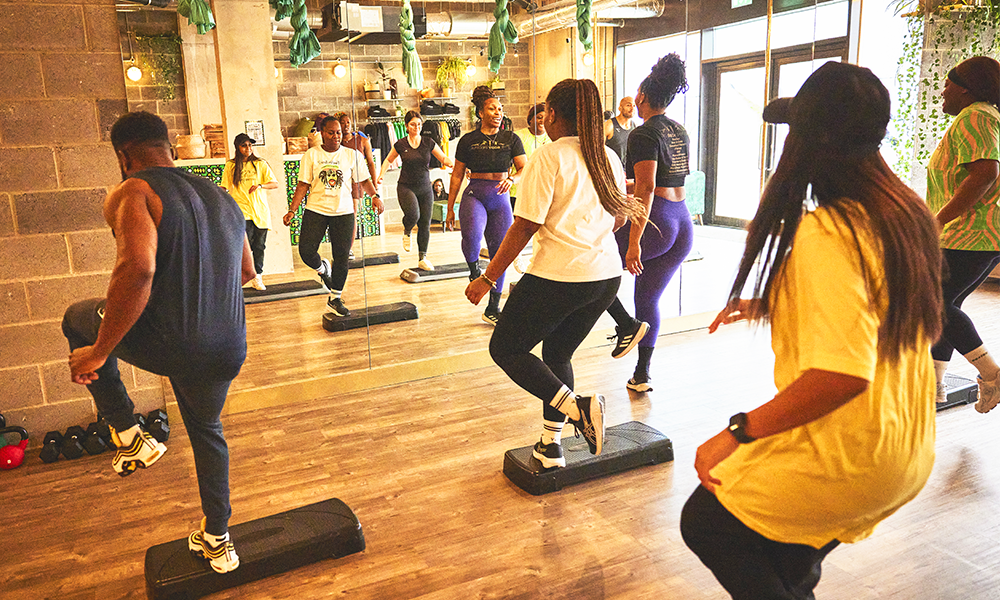 A group of people participate in a step fitness class wearing workout gear and trainers