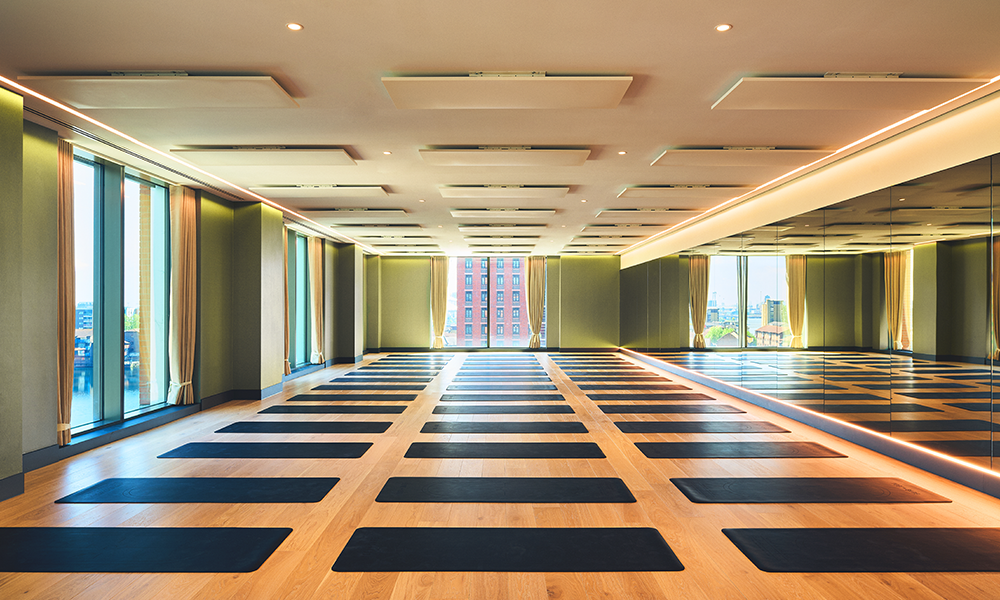 Image shows Third Space Wood Wharf's Hot Yoga studio with black rubber yoga mats on a wooden floor