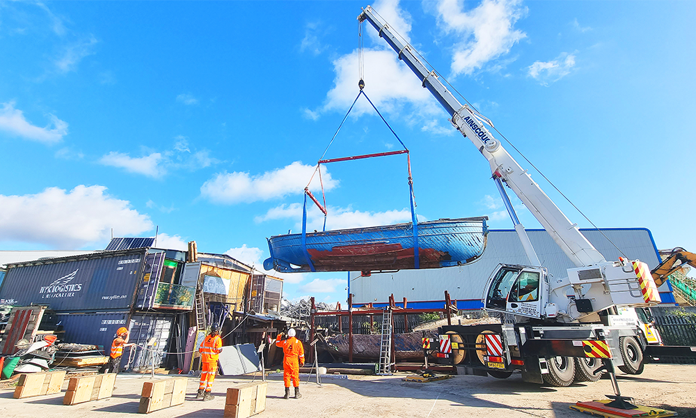 A crane holds the former lifeboat as she is moved to a special shed for refurbishment works