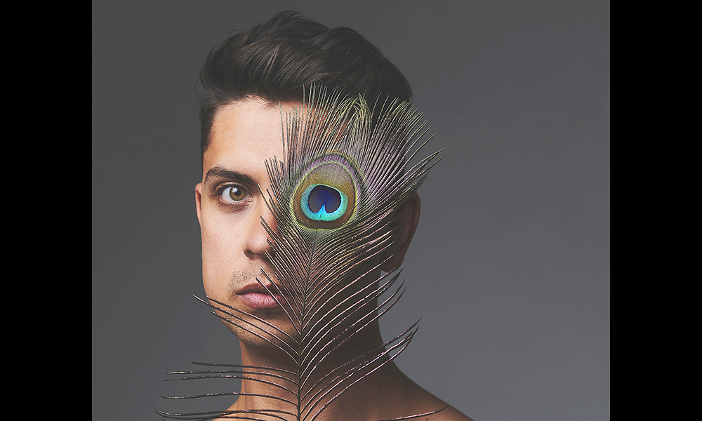 Image shows magician Ben Hart, a man with short dark hair covering one eye with a brightly coloured peacock feather