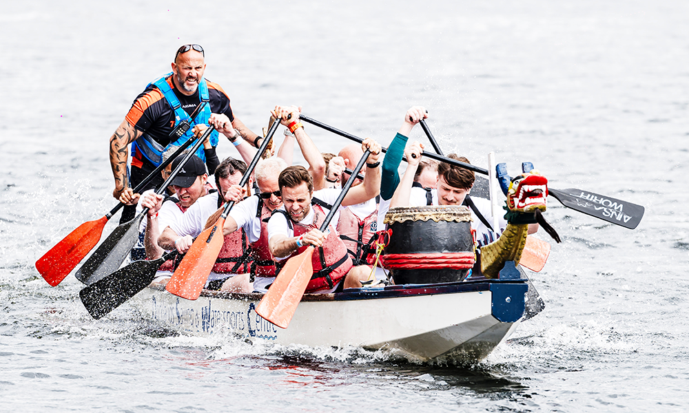 A team competes in the Far East Consortium Dragon Boat Race, flailing paddles at the waters of Millwall Outer Dock