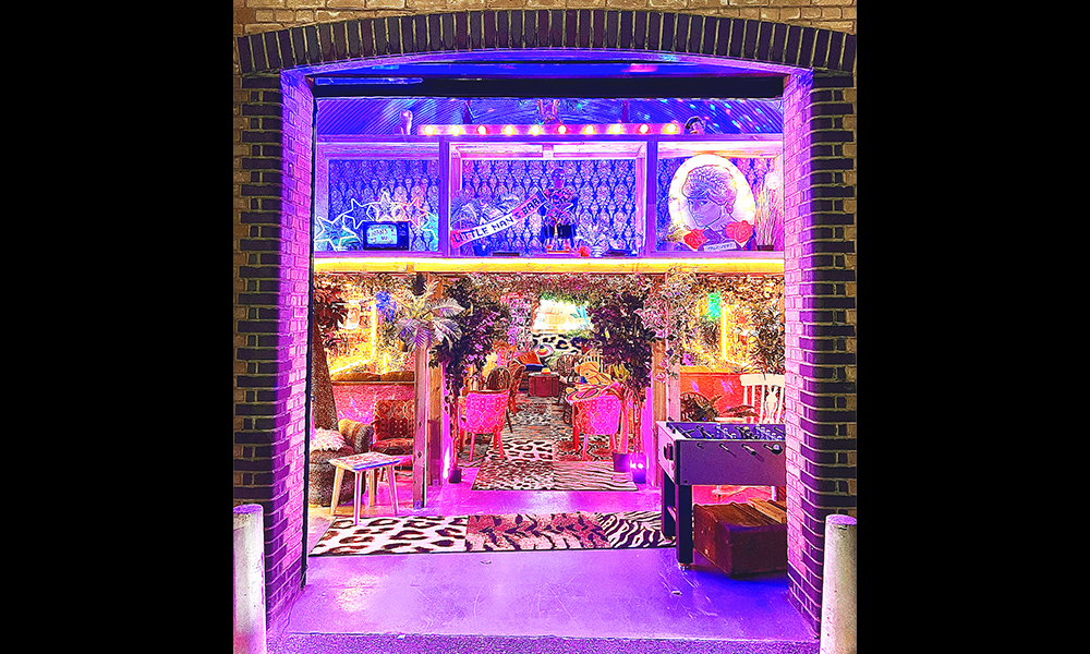 Image shows entry to a brightly lit bar with animal print rugs and neon signs inside