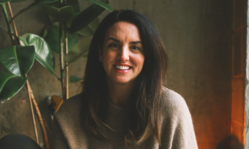 Image shows Hum Yoga + Meditation founder Oriana Shepherd, a woman in a beige jumper with long brunetter hair