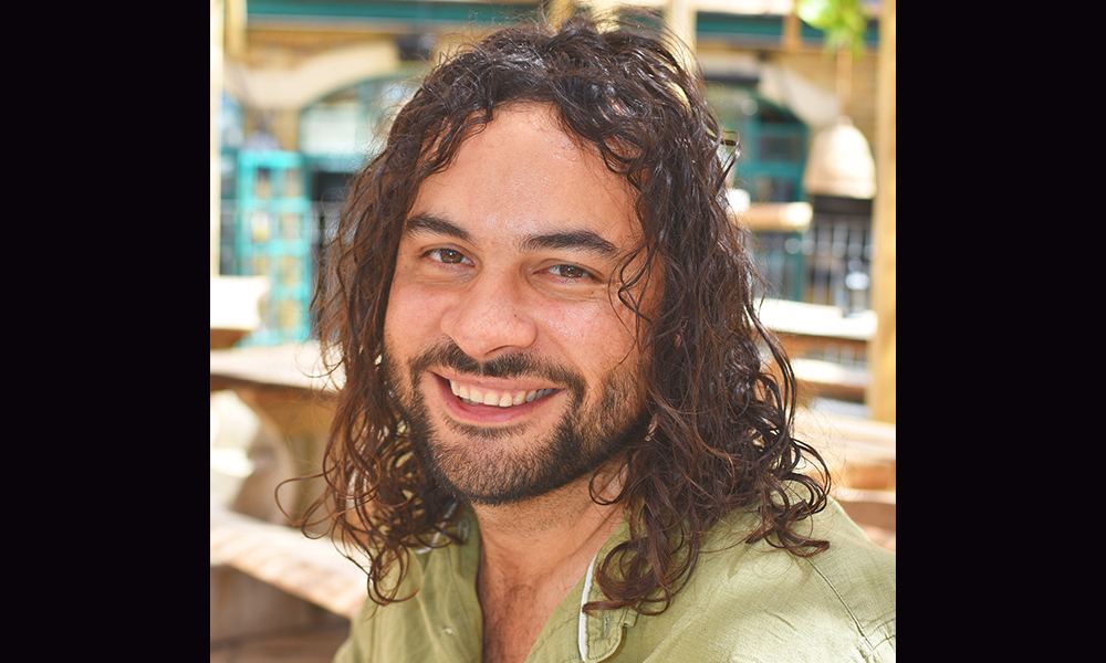 Image shows Toby Kidman, a man with long curly hair, wearing a green shirt - founder of the Pacific Tavern