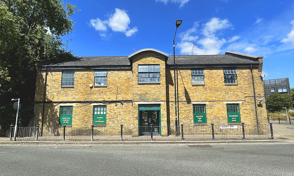 Image shows a honey coloured two storey brick building with green windows - the Pacific Tavern pub