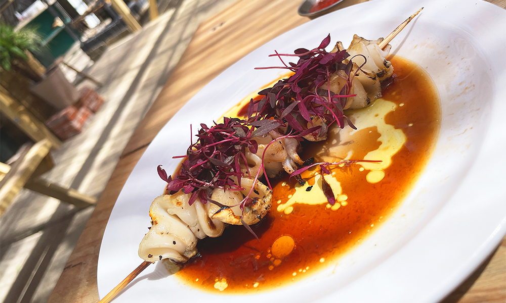 Grilled squid at the pub on a plate covered in purple herbs 