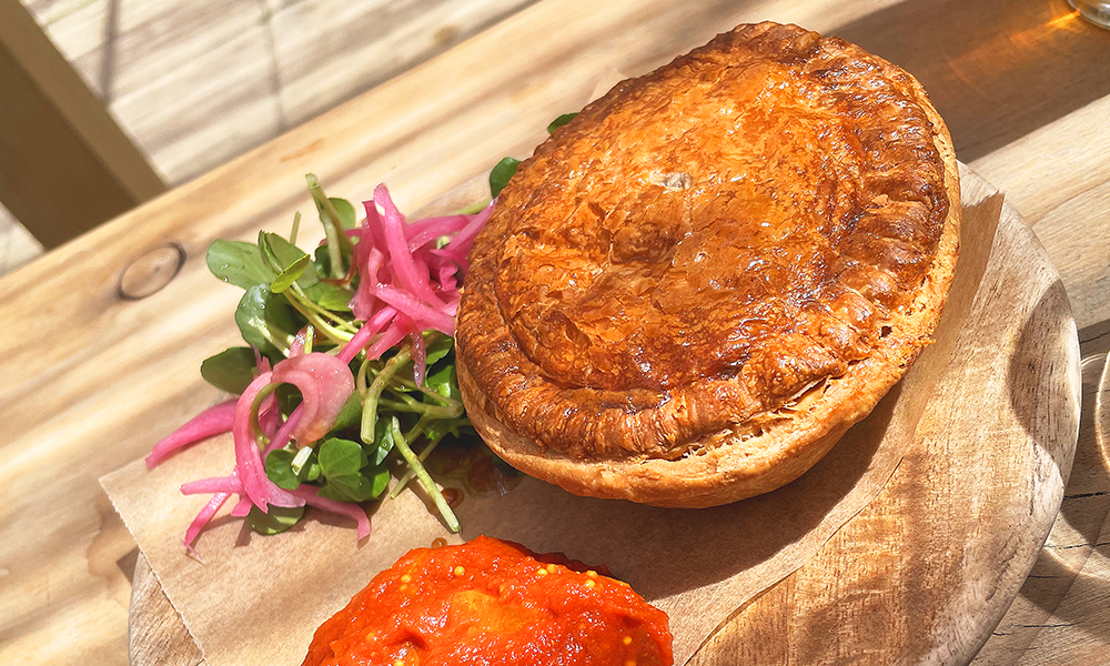 Image shows a puff pastry pie on a wooden block with a red relish and salad