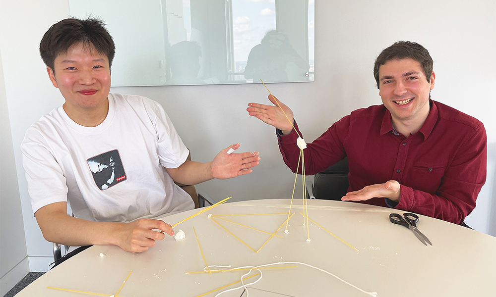 Two men sit either side of a tower of dried spaghetti, marshmallow and tape they have just built as part of an experiment at UCL School Of Management's Behavioural Research Lab in Canary Wharf