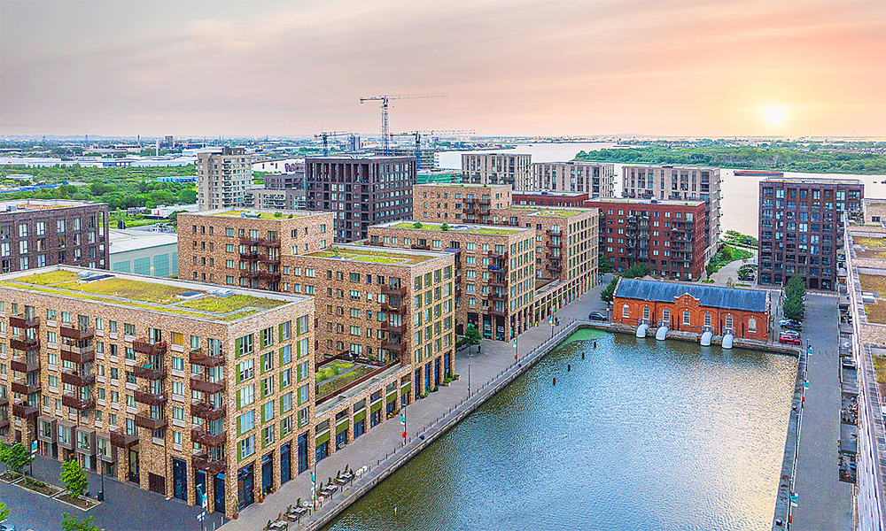 Image shows Royal Albert Wharf at sunrise with the Royal Albert Docks impounding station in view. The buildings are brick-clad and around six storeys high