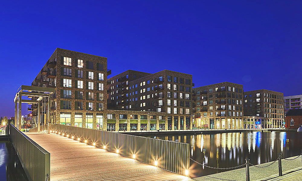 Image shows Royal Albert Dock at night with lights reflected in the waters of the dock