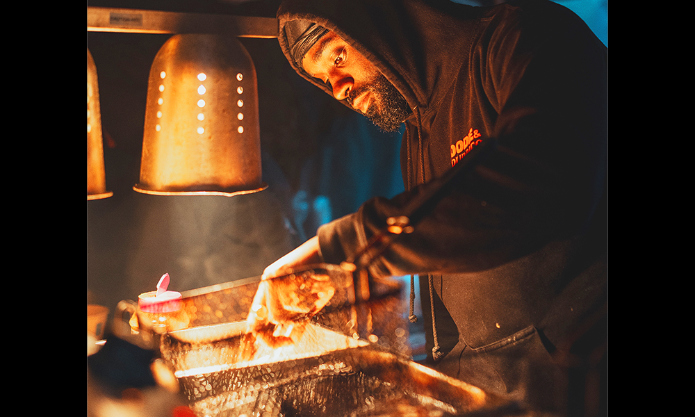 Image shows a man in a hood cooking food at Black Eats Fest