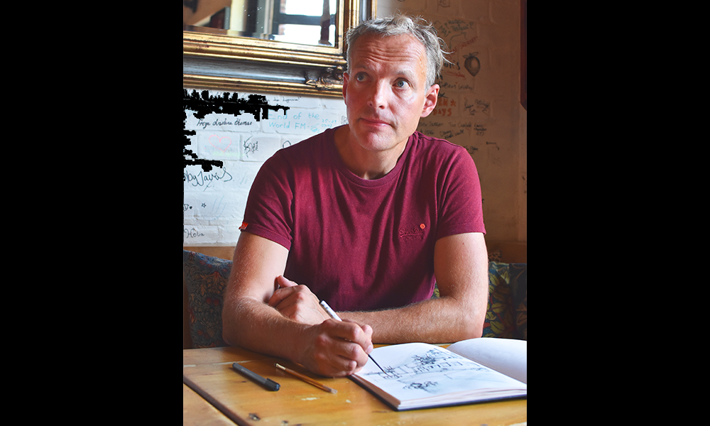 Image shows Ed J Bucknall sketching in The Space Bar – a man in a red T-shirt with grey hair