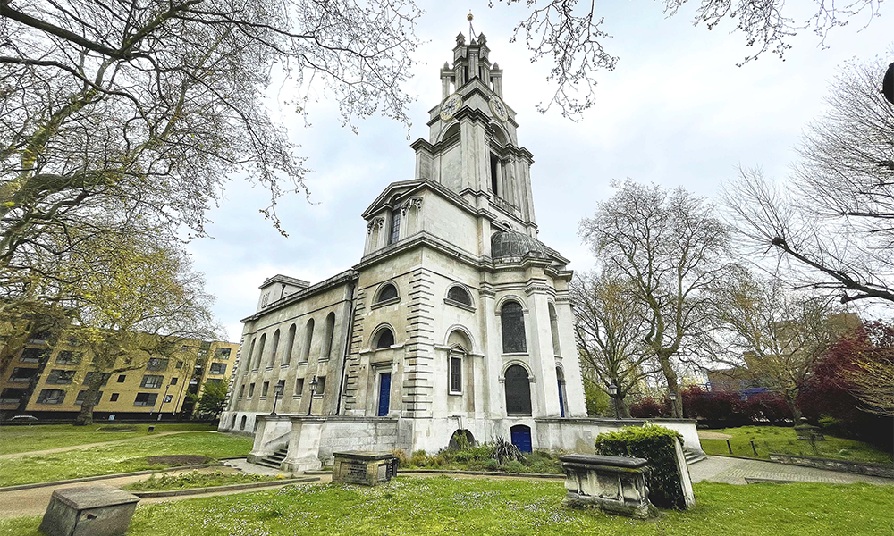 Image shows St Anne's church in Limehouse, a white building surrounded by green lawns