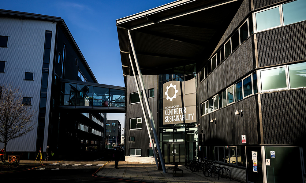 Image shows the Royal Docks Centre For Sustainability at UEL, an angular building with a black clad and glass exterior