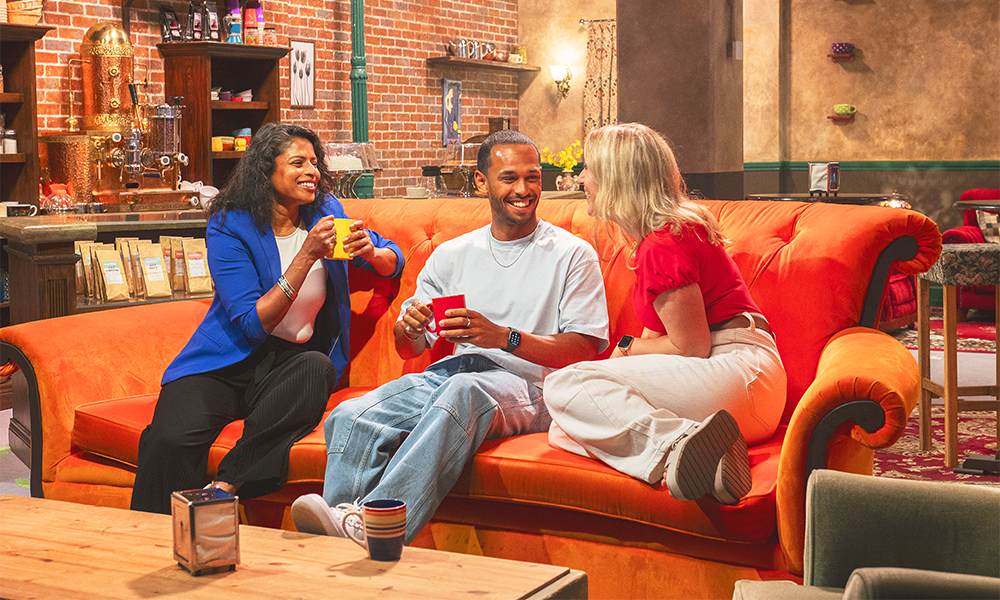 Image shows three people posing with mugs on the Friends sofa at Central Perk