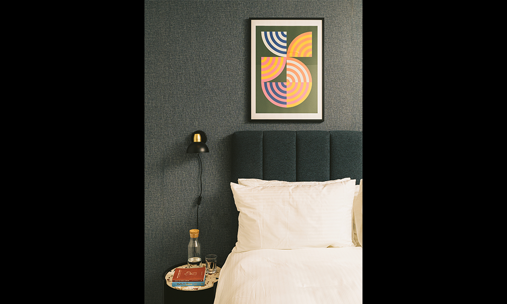 Image shows a bed, with an abstract picture on the wall as well as a reading light