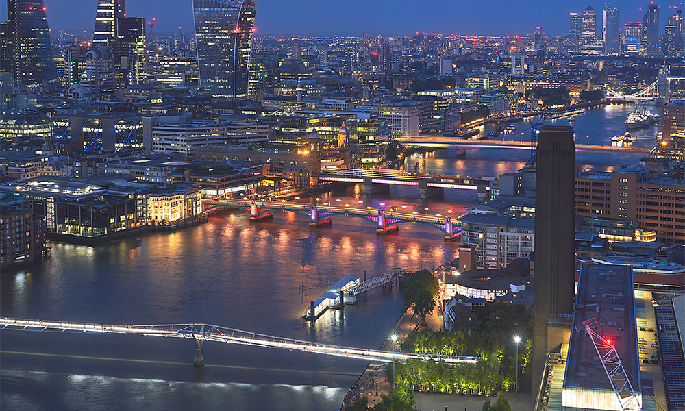 Image shows bridges over the River Thames in central London lit up in bright colours at night