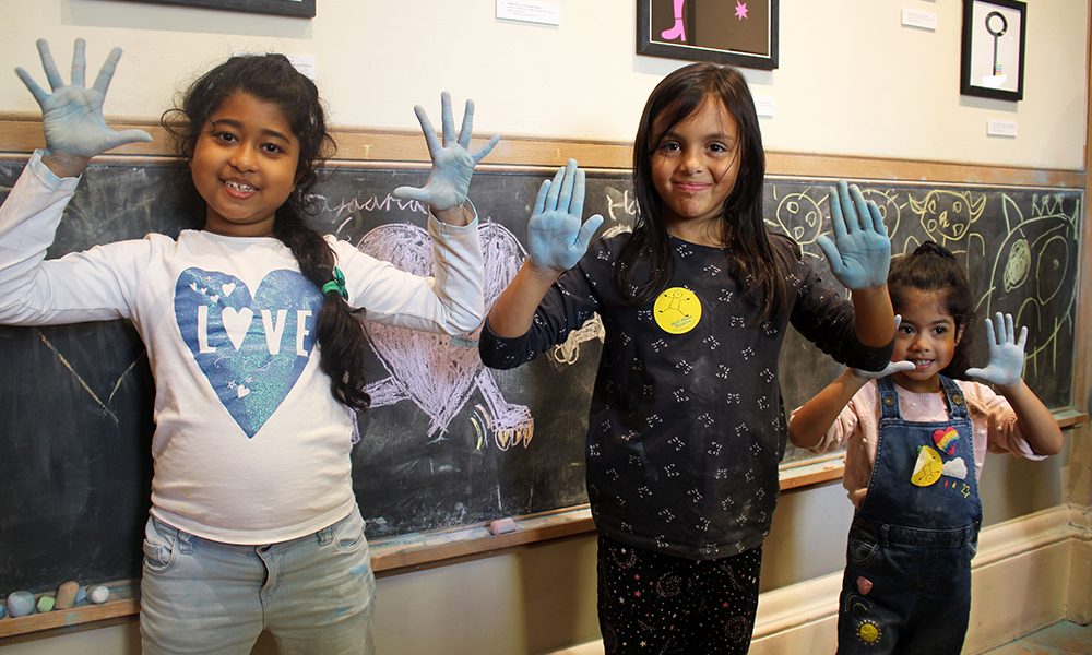 Image shows three children with chalk on their hands at Half Moon Theatre in Limehouse