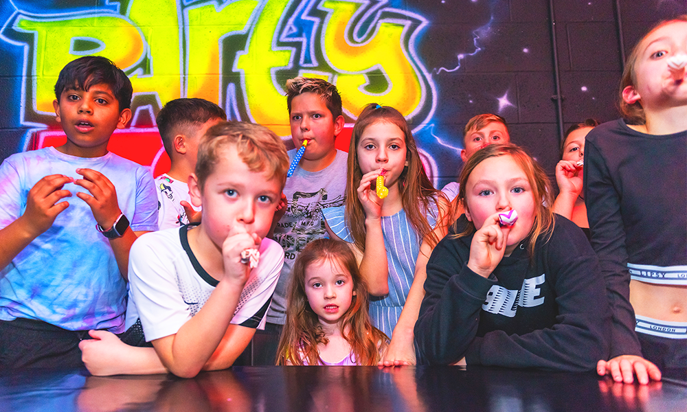 Image shows kids blowing party blowers in a party room at a branch of Laser Quest