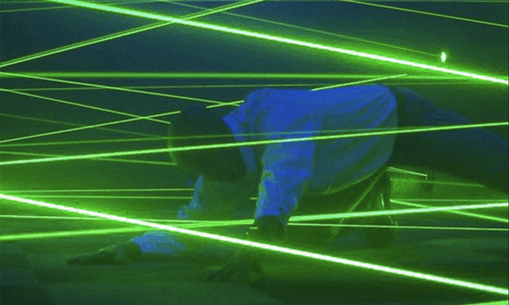 Image shows a man trying to avoid green laser beams in a room