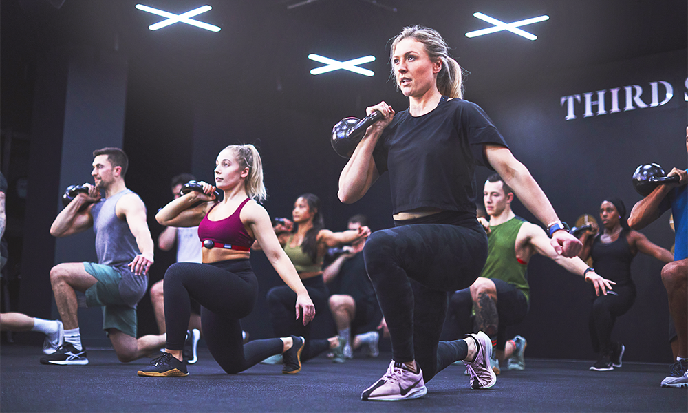 
Members take part in a Lift class at Third Space Canary Wharf - men and women lifting kettlebells while doing lunges