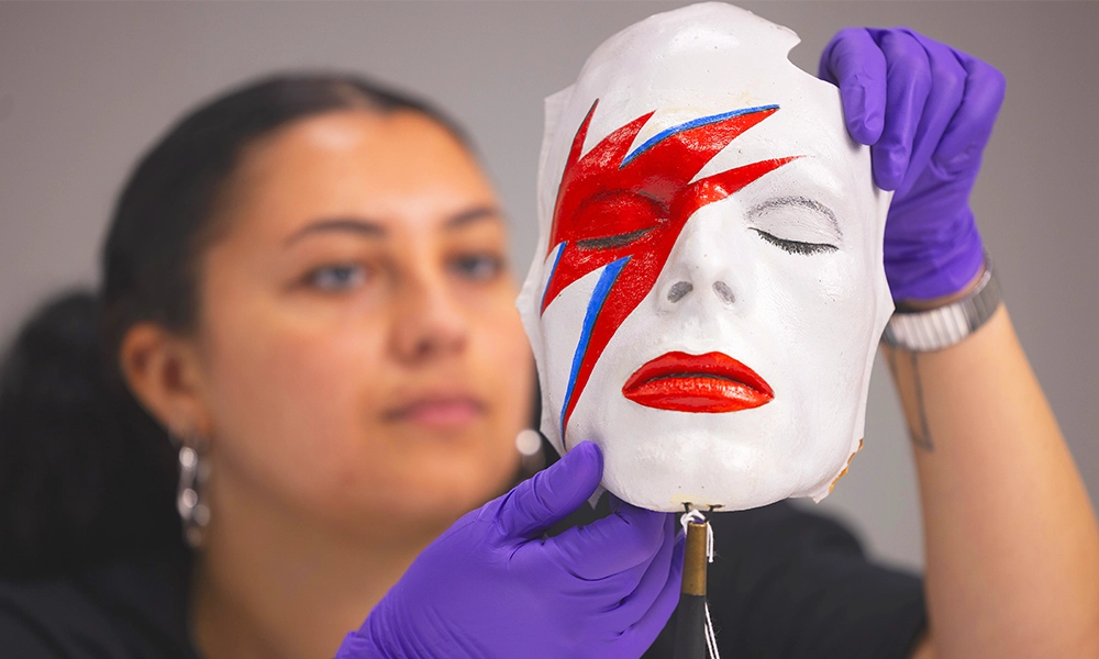 A V&A Collections Access Officer handles a life mask by William Forsche of David Bowie’s face painted to resemble his makeup from Aladdin Sane – image by David Parry for the V&A